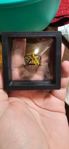Customer holding a personalized black and gold D20 dice in its display case, showing the custom engraved face.