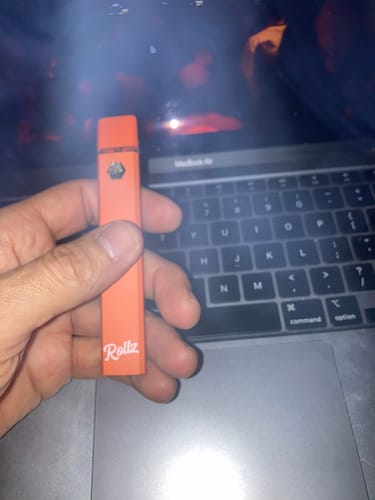 Customer holding the orange ROLLZ THCA Vape in their hand in front of a laptop.