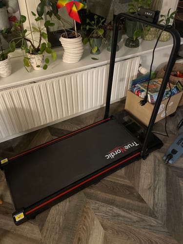 Anmelderens sorte TrueNordic Luksus Løbebånd opstillet i et værelse foran et vindue.