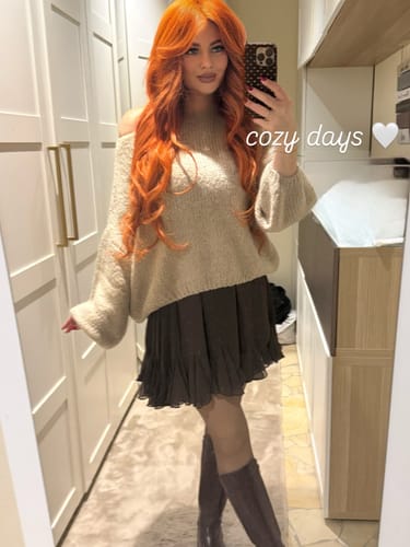 Rezensentin trägt den beigen, lässigen Off-Shoulder-Pullover in Kombination mit einem dunklen Rock und Stiefeln.