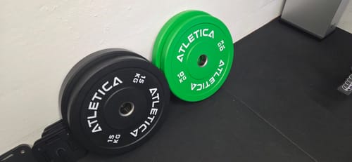 Kunde zeigt eine schwarze 15-kg- und eine grüne 10-kg-Color-Bumper-Plate auf einer Matte.