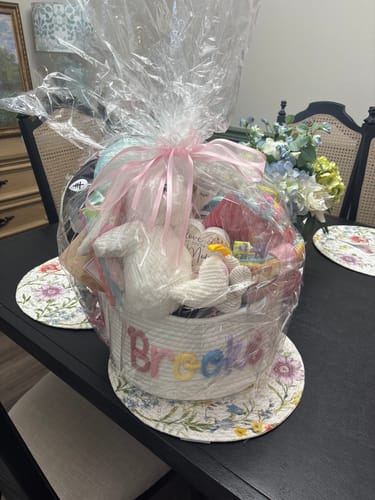 Reviewer's large woven basket, personalized and filled with baby shower gifts, wrapped in cellophane.