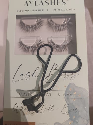 Ein Rezensent zeigt die schwarze AYLASHES Wimpernzange auf der dazugehörigen Produktverpackung.