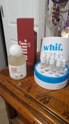 Customer's Vivid Haze perfume bottle and its red box displayed on a wooden table next to a perfume sampler set.