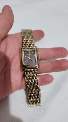 Customer's hand holding the Olivia Gold Brown watch, showing its rectangular brown face and gold mesh band.