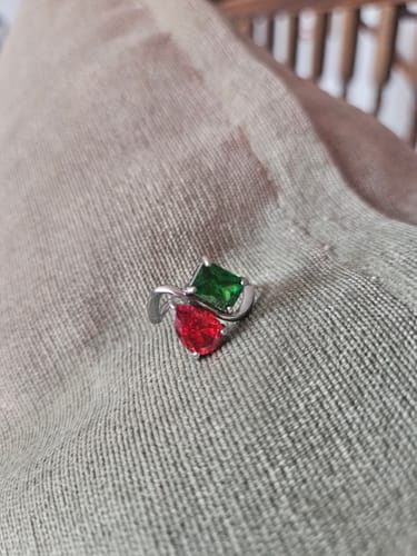 Customer's Navae Birthstone Ring with a red pear-cut stone and a green radiant-cut stone, resting on grey fabric.