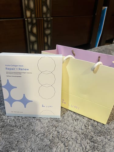 Reviewer's packaging for the Hydra Collagen Mask displayed next to a branded shopping bag on a carpet.