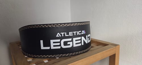 Ein Kunde zeigt den schwarzen Legend Gewichtheber-Gürtel mit weißen Nähten auf einem Holzregal.