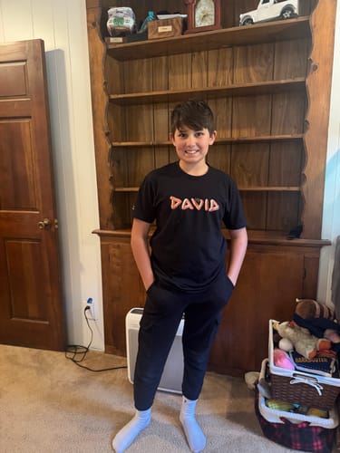 Customer's photo of a smiling young person wearing the black DAVID Logo T-Shirt.