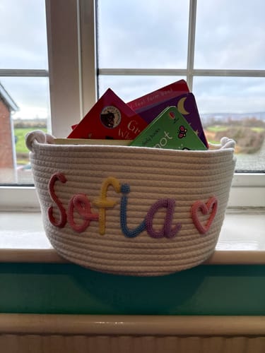 Reviewer's personalized basket, woven from rope, with the name 'Sofia' in colorful yarn, filled with books.