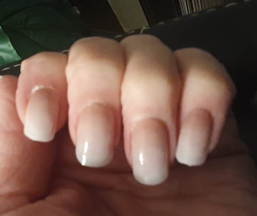 Hand eines Kunden mit manikürten Nägeln, die glänzende Nagelfolien im Ombré-Stil zeigen.