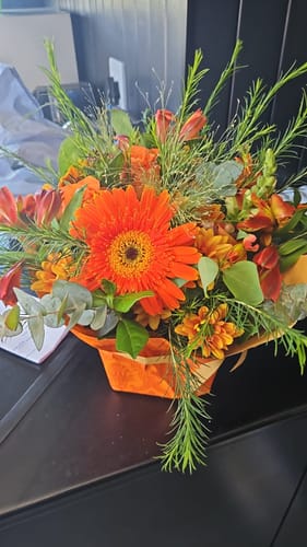 Reviewer's Celebrate Flower Arrangement featuring a large orange gerbera, mixed flowers, and lush greenery.