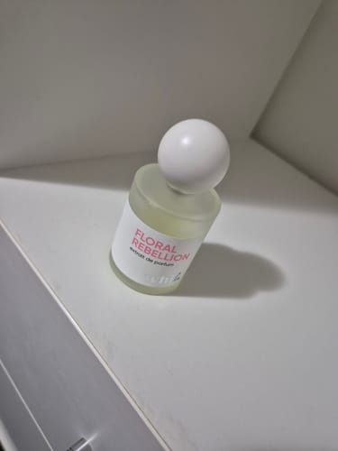 A customer's bottle of Floral Rebellion perfume with its spherical white cap, resting on a clean white surface.