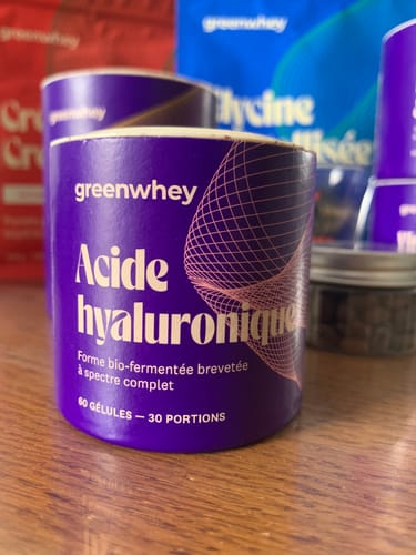 Gros plan sur le pot violet d'Acide hyaluronique du client, posé sur une table en bois.