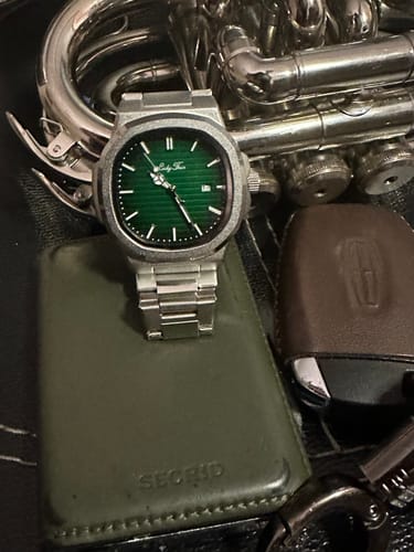Customer's Lucky Fours® Caspian watch with a green face, resting on a wallet next to other personal items.