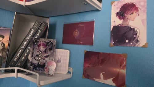 Customer's Penelope's Pendant and surprise art cards displayed on a white shelf with other series merchandise.