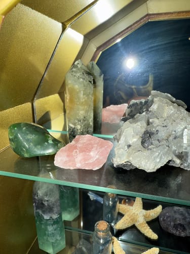 Reviewer's raw rose quartz from the VIP Crystal Club sitting on a glass shelf with other collected crystals.