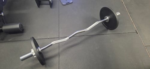 Rezensentenfoto der SZ Stange mit schwarzen Hantelscheiben, die auf einem dunklen Fitnessboden liegt.