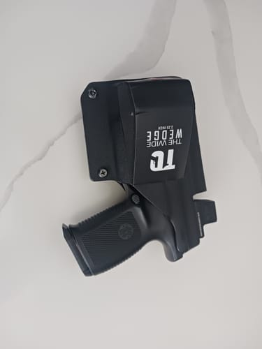 Customer's black T1C 2.25 Inch Wide Wedge installed on a Kydex holster with a pistol, viewed from the side on a marble surface.