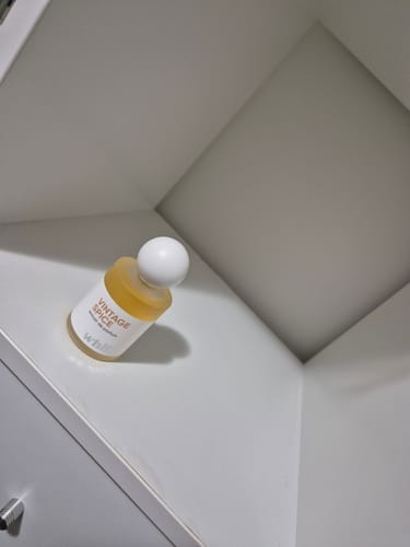 Reviewer's bottle of Vintage Spice perfume with a spherical white cap, sitting in the corner of a cabinet.