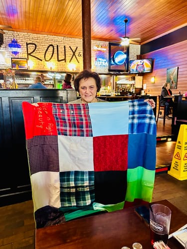 Customer holds up a large Premium T-Shirt Quilt made of colorful patchwork squares at a restaurant table.