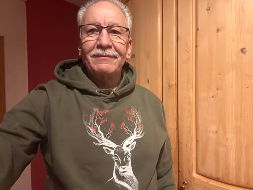 Ein Kunde trägt den olivgrünen HIRSCH BLÜTEN Bio Unisex Hoodie mit einer Hirsch-Grafik.