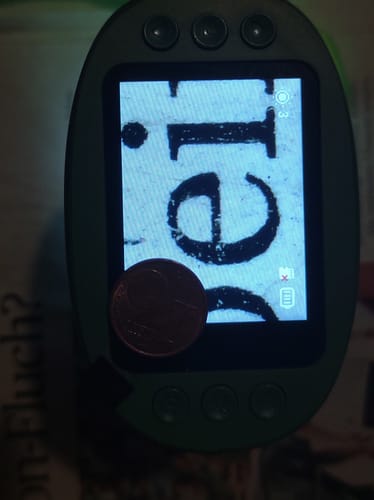 Kunde zeigt vergrößerte Buchstaben auf dem Bildschirm des Edubini Abenteuer-Mikroskops, mit einer Münze zum Größenvergleich.