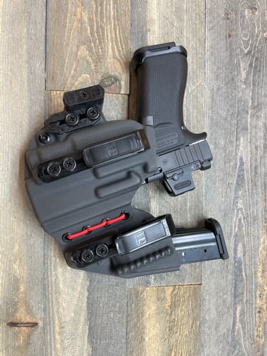 Reviewer's black AXIS ELITE holster with red shock cord, holding a firearm and spare magazine on a wood surface.