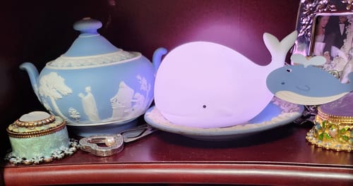 Customer's MINIMI WHALE SILICON MOOD LAMP glowing with a purple light on a shelf next to decorative items.