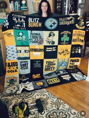 Customer holding up a large, custom Premium T Shirt Quilt made from many Pittsburgh Steelers themed shirts in their home.