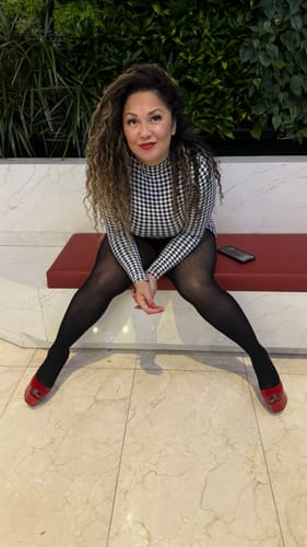 Reviewer sitting on a bench wearing the long-sleeved Naked Print Mini Dress with black tights.