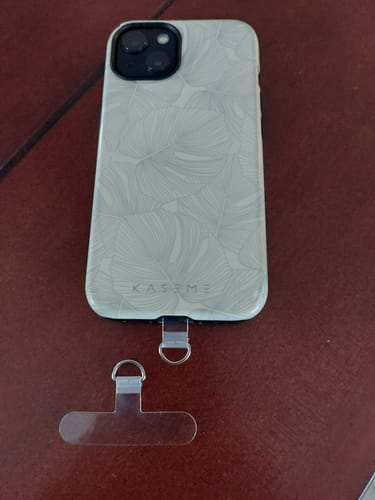 Reviewer showing one Crossbody Strap plastic tab installed in a phone case, with a second tab lying next to it on a table.