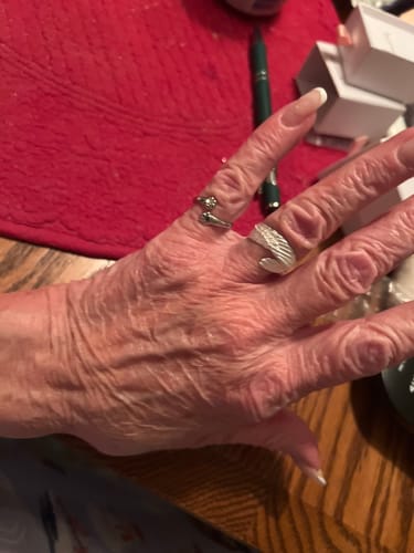 A customer's hand wearing the Guardian Angel Ring, which is shaped like a textured silver wing, on the middle finger.