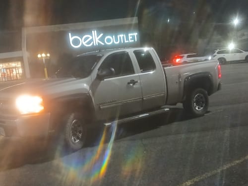 Customer's silver Silverado with the leveling lift kit installed, seen from a front-quarter angle in a parking lot at night.