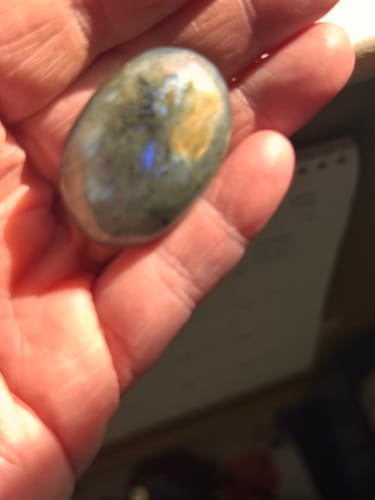 Close-up of a customer holding a polished labradorite crystal in their palm, showing blue and gold flashes.