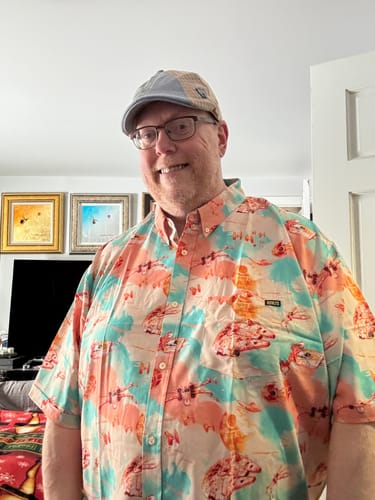 Reviewer smiling while wearing the colorful 'Cosmic Crossfire' Star Wars shirt indoors.