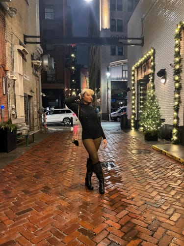 Customer posing in a brick alley at night wearing the sparkling Crystal Turtleneck Romper.