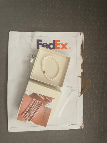 Reviewer's Mother of Pearl accent bracelet displayed in its open box on top of a FedEx mailer.