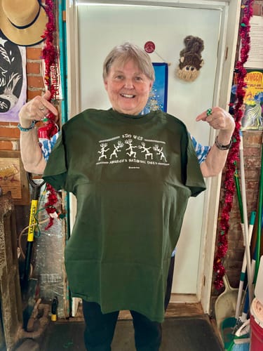 Reviewer happily holding up the green Stay Wild Petroglyphs Tee.