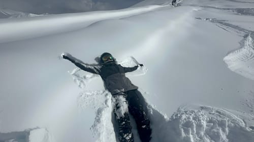 Reviewer making a snow angel in deep snow while wearing the baggy waterproof snow pants.
