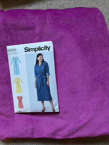 Reviewer shows the grape corduroy fabric with a utility dress sewing pattern resting on top.