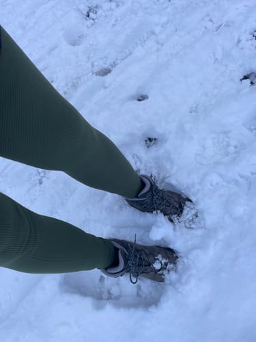 Kundin steht mit einer grünen Tofana-Leggings und Wanderschuhen im Schnee.