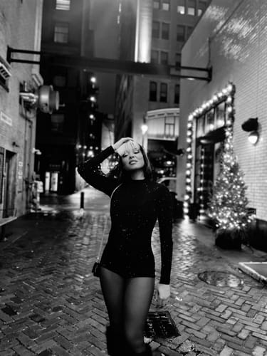 Black and white photo of a reviewer posing in the Crystal Turtleneck Romper in an alley at night.