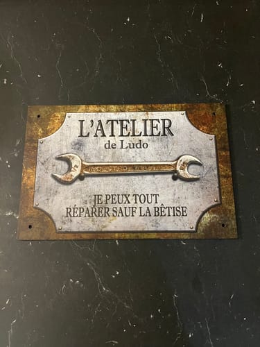 Un client montre sa pancarte personnalisée de style rustique, indiquant 'L'ATELIER de Ludo'.