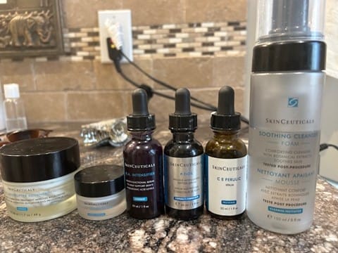 Reviewer's SkinCeuticals HA Intensifier serum in a purple bottle, shown with other skincare products on a counter.