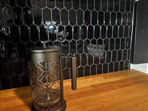 Nærbilde fra anmelders kjøkken som viser en kaffepresse foran en svart, flislagt vegg.