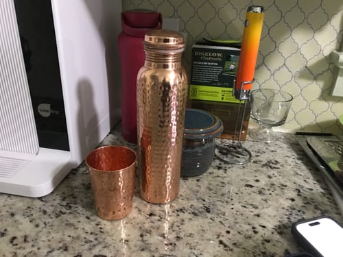 Customer's hand-hammered Pure Copper Water Bottle and a matching cup sitting on a kitchen counter.