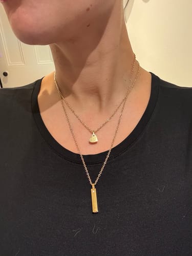 Customer wearing a gold Minimal Stone-Set Urn Pendant layered with a shorter, smaller urn necklace on a black shirt.