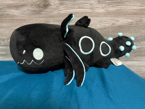 Customer's black Rain World Glowing Cyan Lizard Plush with bright cyan details, resting on a blue surface.