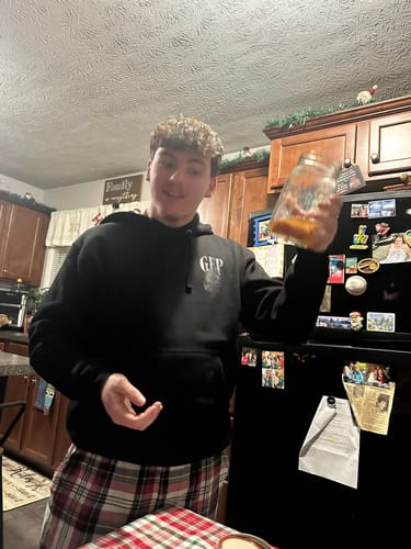 Customer wearing the black ROSE HOODIE with a white chest logo in a kitchen.